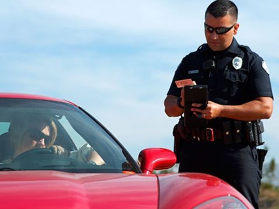 police officer giving a blonde woman a ticket in a red car.